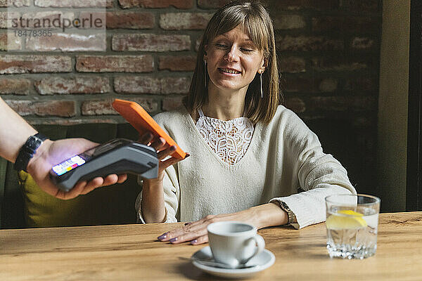 Lächelnde Frau  die im Café per Smartphone bezahlt