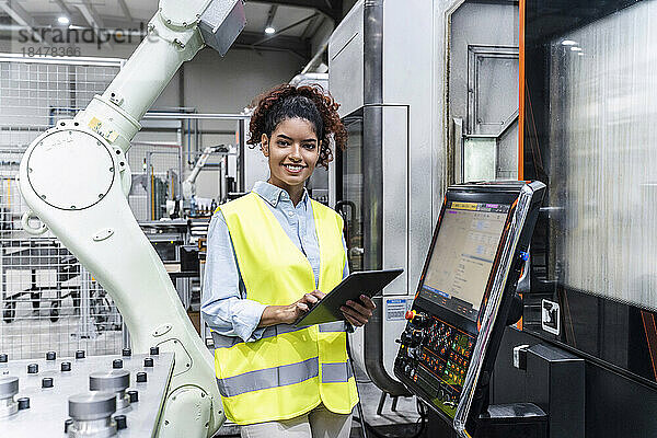 Glücklicher Ingenieur steht mit Tablet-Computer neben der Maschine in der Fabrik