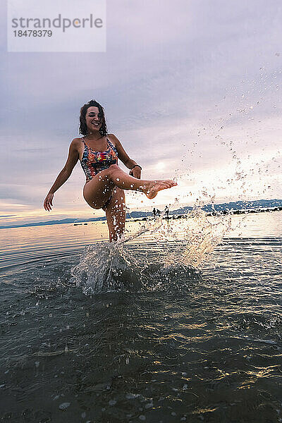 Glückliche junge Frau  die am Strand Wasser spritzt