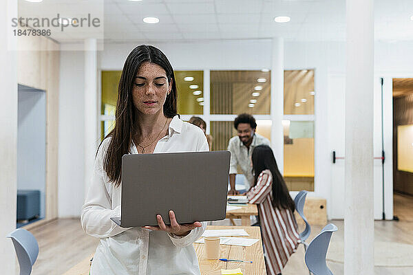 Geschäftsfrau benutzt Laptop im Büro mit Kollegen im Hintergrund