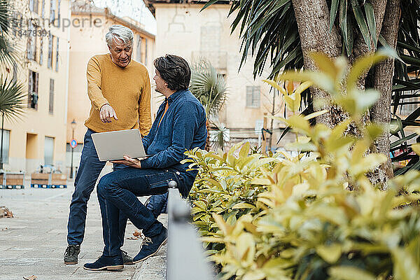 Vater und Sohn diskutieren am Laptop vor dem Gebäude