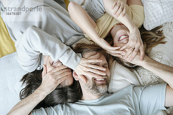 Playful family covering each others faces lying at home