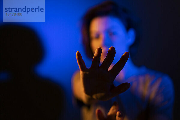 Frau gestikuliert in blauer Neonbeleuchtung vor farbigem Hintergrund