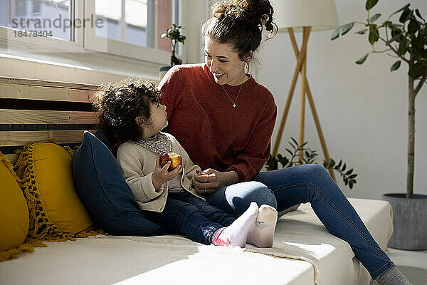 Mutter sitzt auf Sofa und Tochter isst Apfel