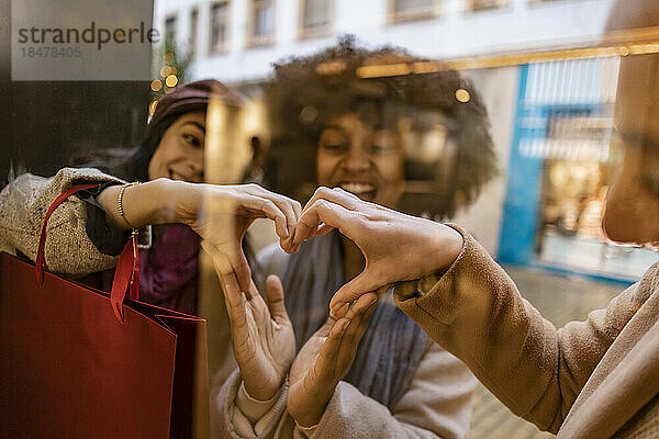 Fröhliche junge Freunde formen gemeinsam ein Herz mit Händen  die durch Glas gesehen werden