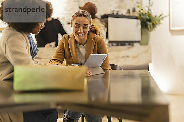 Lächelnde Freunde  die am Tisch im Café sitzen und einen Tablet-PC nutzen