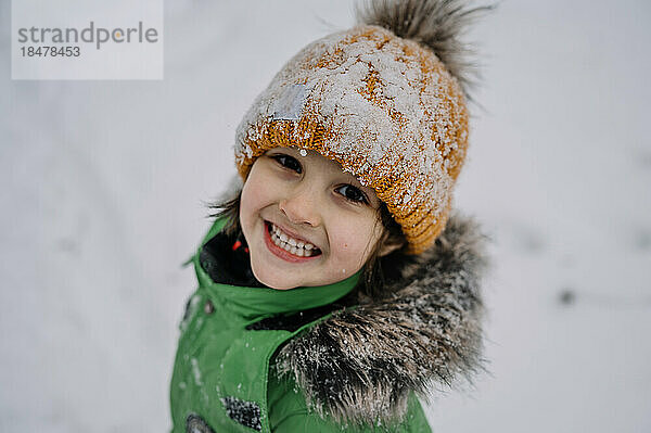 Netter Junge mit Strickmütze spielt im Schnee