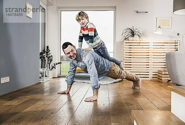 Junge balanciert auf dem Rücken seines Vaters und macht Liegestütze im heimischen Wohnzimmer