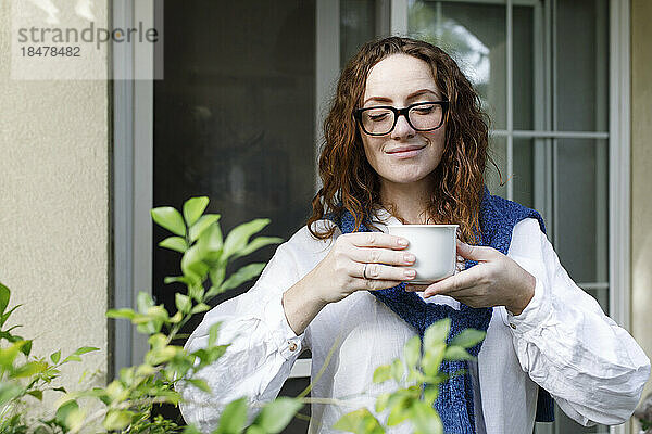 Lächelnde Frau mit Brille und Tasse Tee im Hinterhof