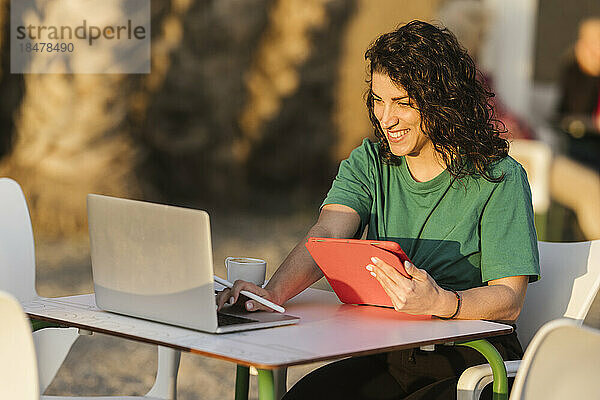 Glückliche Frau sitzt mit Laptop im Straßencafé