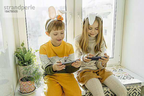 Happy girl and boy playing video games on smart phone at home