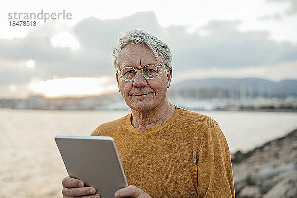 Lächelnder älterer Mann steht mit Tablet-Computer