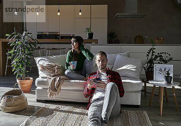 Mann und Frau sitzen mit Getränken im Wohnzimmer zu Hause