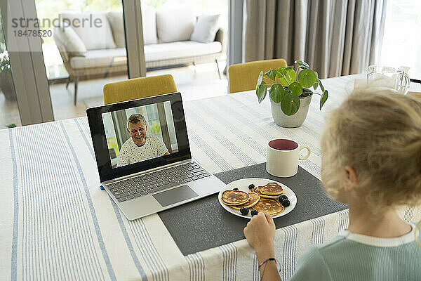 Mädchen macht Videoanruf mit Großvater über Laptop zu Hause