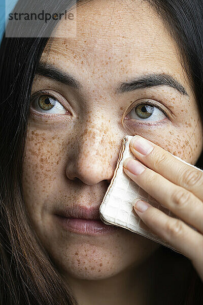 Woman with freckles cleaning face with makeup wipe