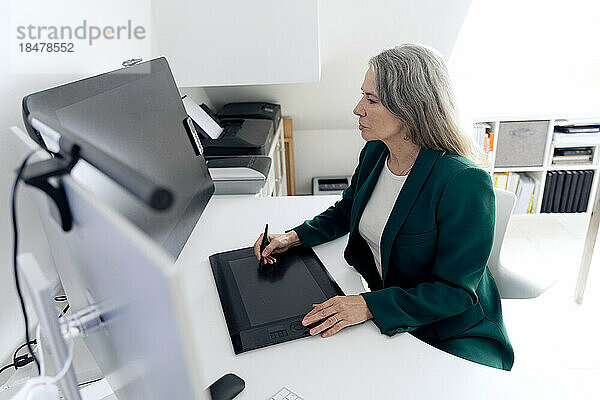 Geschäftsfrau mit Grafiktablett sitzt am Schreibtisch im Büro