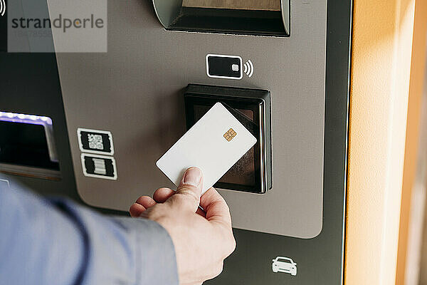 Hand eines Geschäftsmannes mit Kreditkarte am Fahrkartenautomaten
