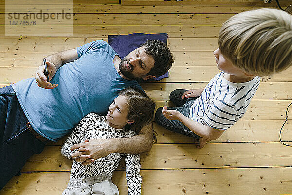 Father sharing smart phone with daughter and son lying on floor at home