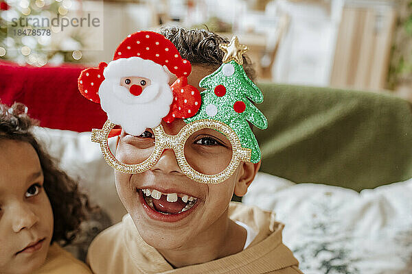 Fröhlicher Junge mit Weihnachtsbrille und Schwester zu Hause