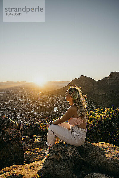 Frau sitzt bei Sonnenaufgang auf einem Felsen