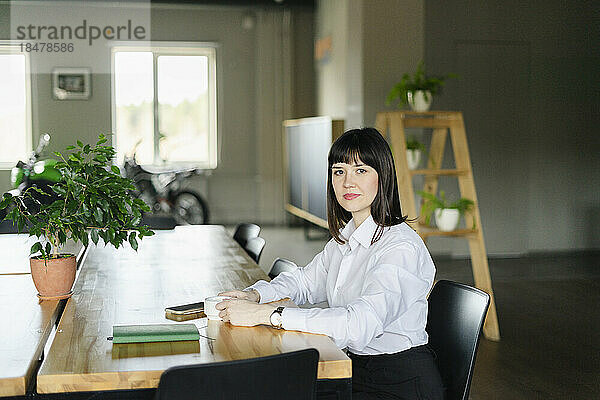 Porträt einer selbstbewussten brünetten Geschäftsfrau  die im Büro am Tisch sitzt
