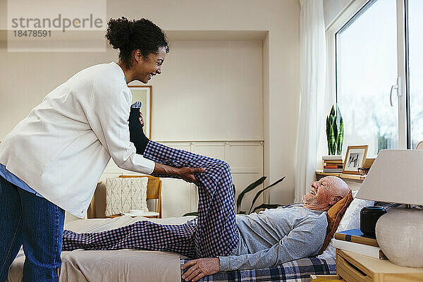 Glücklicher Physiotherapeut hilft älterem Mann bei der Physiotherapie zu Hause