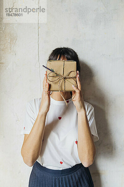 Frau bedeckt ihr Gesicht mit einer Geschenkbox vor der Wand