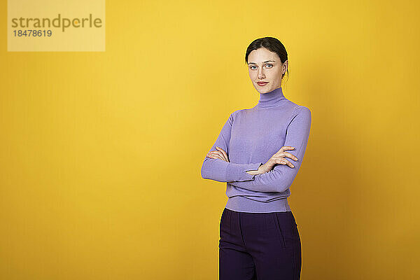 Confident young woman standing against yellow background