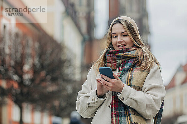 Lächelnde junge Frau  die ihr Mobiltelefon benutzt