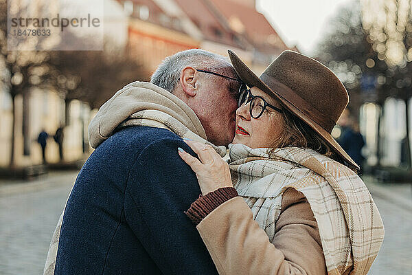Senior man kissing woman wearing hat and scarf