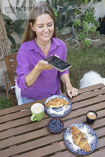 Glückliche Frau macht ein Selfie mit Croissants auf dem Tisch im Garten