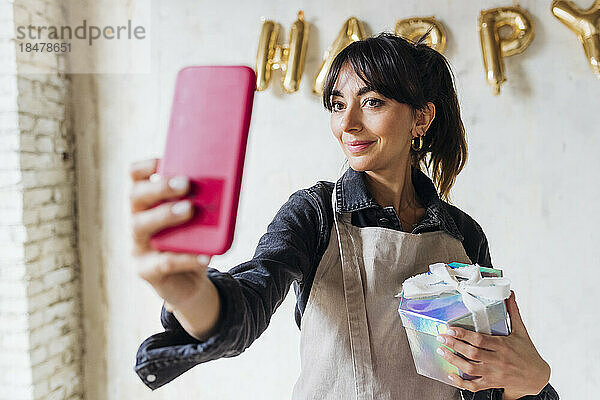 Lächelnde Frau mit Geschenkbox  die ein Selfie mit dem Smartphone macht