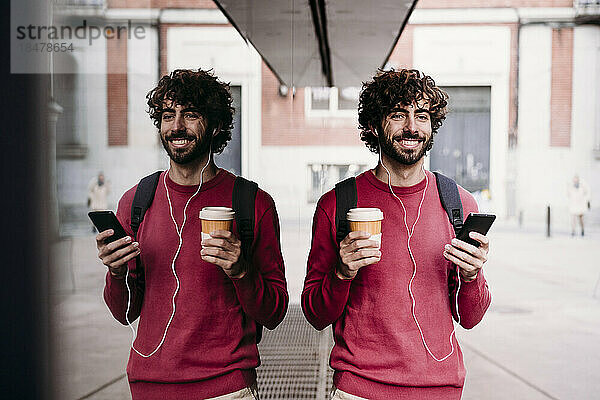 Glücklicher Mann mit Smartphone und Kaffeetasse steht am Fußweg