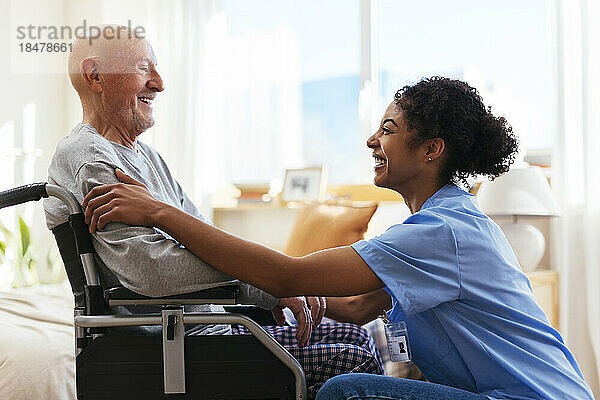 Glücklicher Physiotherapeut  der mit einem älteren Mann spricht  der im Rollstuhl sitzt