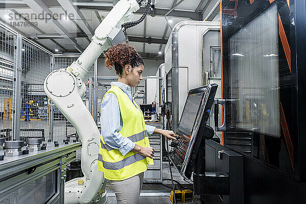 Ingenieur steht neben Roboterarm und Bedienmaschine in der Fabrik
