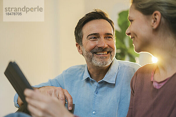 Lächelnder reifer Mann spricht zu Hause mit Frau mit Tablet-PC