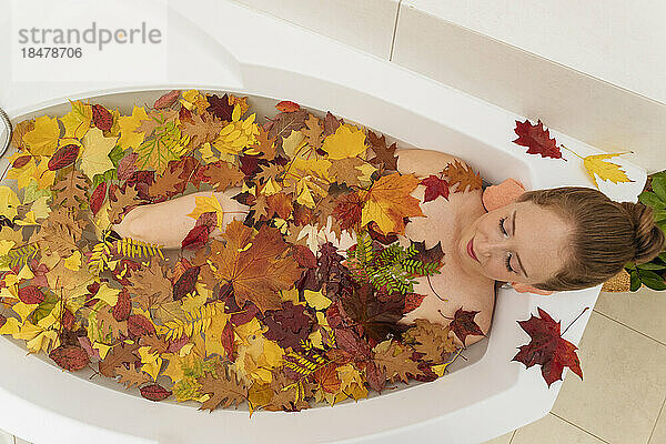 Woman with autumn leaves lying in bathtub