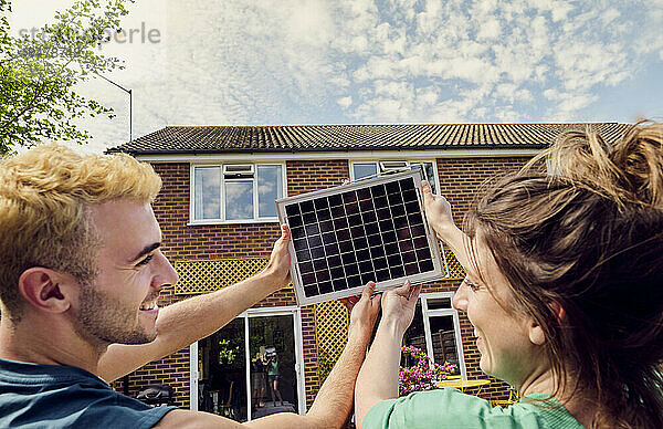 Glückliches Paar hält Solarpanel vor dem Haus