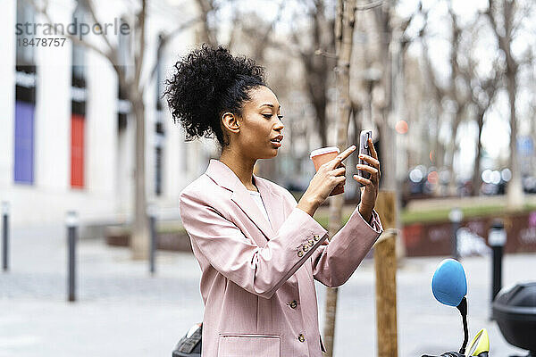 Junge Geschäftsfrau mit Kaffeetasse und Mobiltelefon
