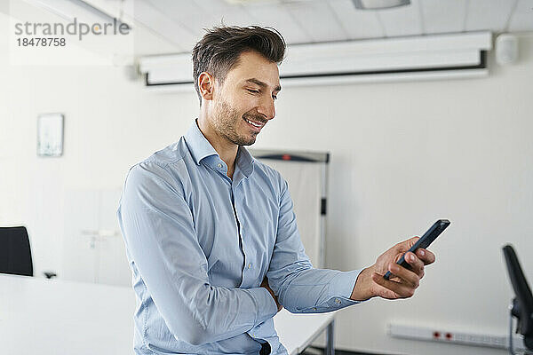 Lächelnder Geschäftsmann  der am Arbeitsplatz sein Mobiltelefon benutzt