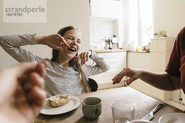 Glückliches Mädchen  das zu Hause beim Frühstück auf dem Tisch lacht