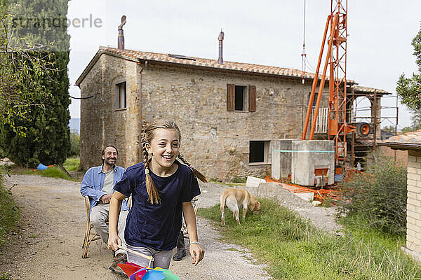 Glückliches Mädchen hält ein Windradspielzeug in der Hand und genießt es  während der Vater im Hintergrund sitzt
