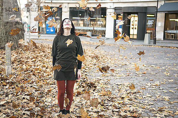 Frau steht inmitten fallender Herbstblätter auf einem Fußweg