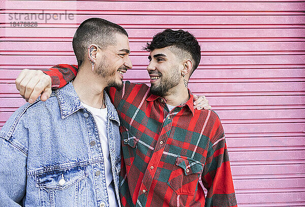 Happy gay couple with arms around standing in front of roller shutter wall