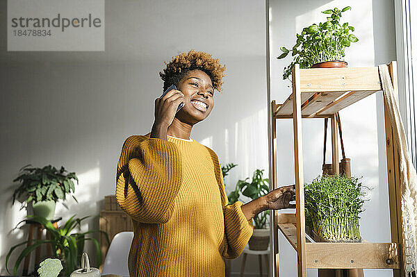 Glückliche Frau  die am Pflanzenregal steht und mit ihrem Smartphone spricht