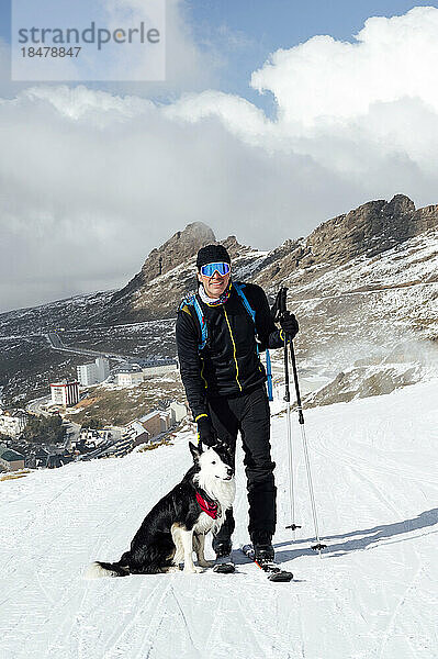Mann steht mit Skistöcken und Hund im Schnee