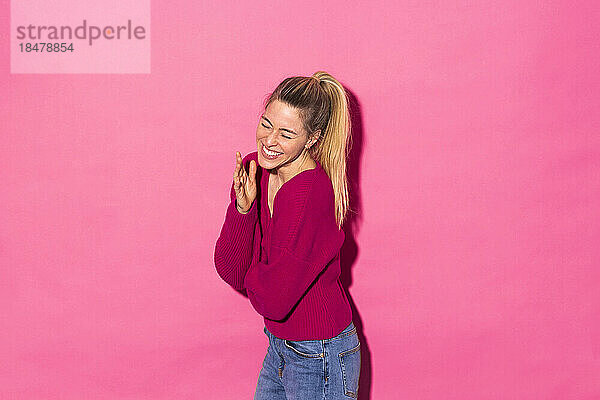Happy woman laughing against pink background