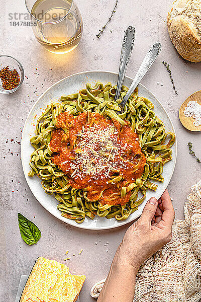 Hand einer reifen Frau mit Spinat-Tagliatelle und Tomatensauce  serviert auf einem Teller auf dem Tisch