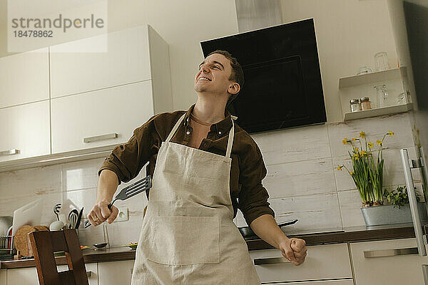 Glücklicher Mann mit Schürze tanzt zu Hause in der Küche
