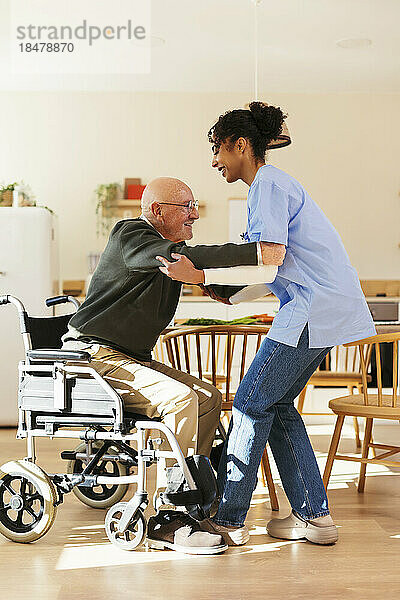 Heimpfleger hilft älterem Mann beim Aufstehen aus dem Rollstuhl